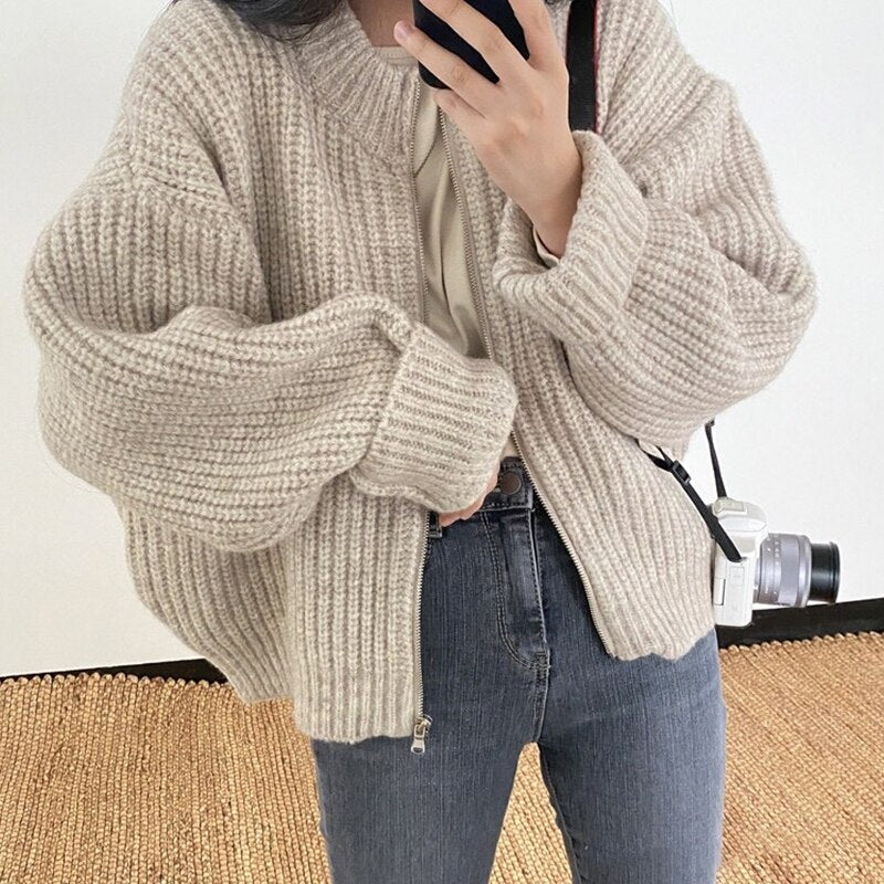 Frau in beiger Strickjacke, Jeans, Kamera; modische Herbstbekleidung, gemütlicher Stil.