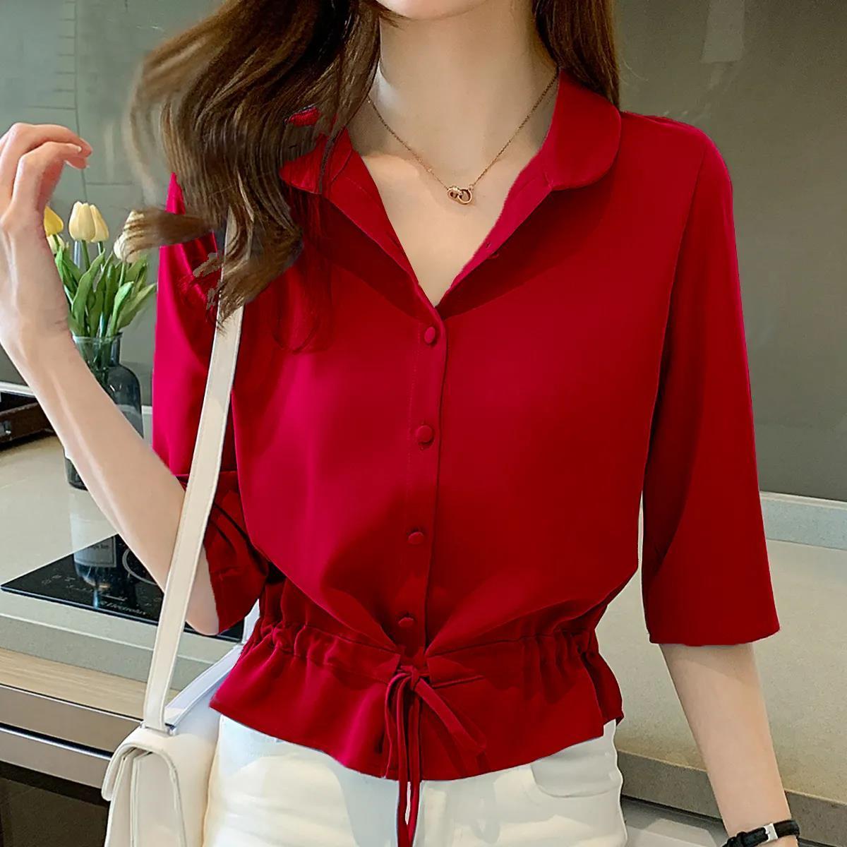Frau in roter Bluse mit Knopfleiste und Kordelzug, weiße Hose, moderne Küche im Hintergrund.