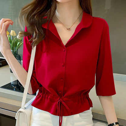 Frau in roter Bluse mit Knopfleiste und Kordelzug, weiße Hose, moderne Küche im Hintergrund.