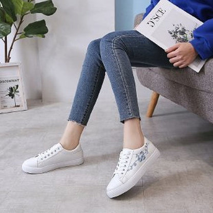 Frau trägt weiße Sneakers mit Blumenmuster, sitzt auf Sofa, blaue Jeans, lässiger Stil.