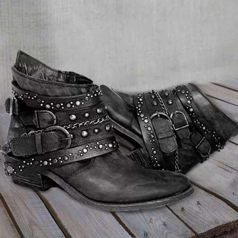 Schwarze Lederstiefeletten mit Nieten und Schnallen, Damenmode, Vintage-Stil, auf Holzboden.