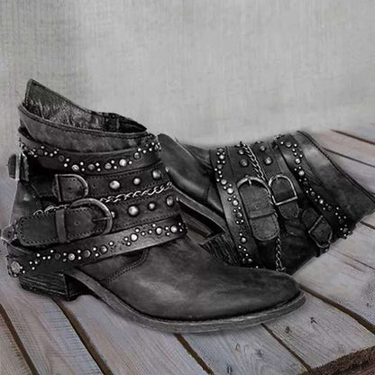 Schwarze Lederstiefeletten mit Nieten und Schnallen, Damenmode, Vintage-Stil, auf Holzboden.