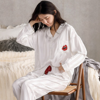 Frau in weißem Pyjama mit Lippenmotiv, sitzt auf Stuhl, gemütliche Schlafzimmeratmosphäre.