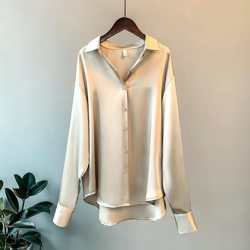 Beige Damenbluse aus Satin, langärmelig, mit Knopfleiste, elegantes Design, auf Kleiderbügel.
