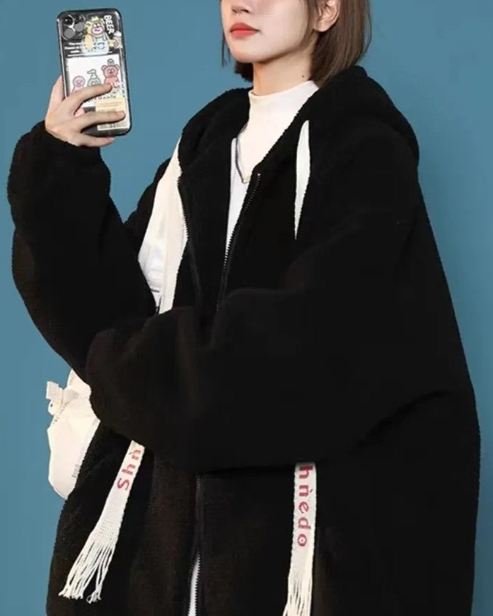 Frau in schwarzer Teddyjacke mit Kapuze, Smartphone in der Hand, blauer Hintergrund.