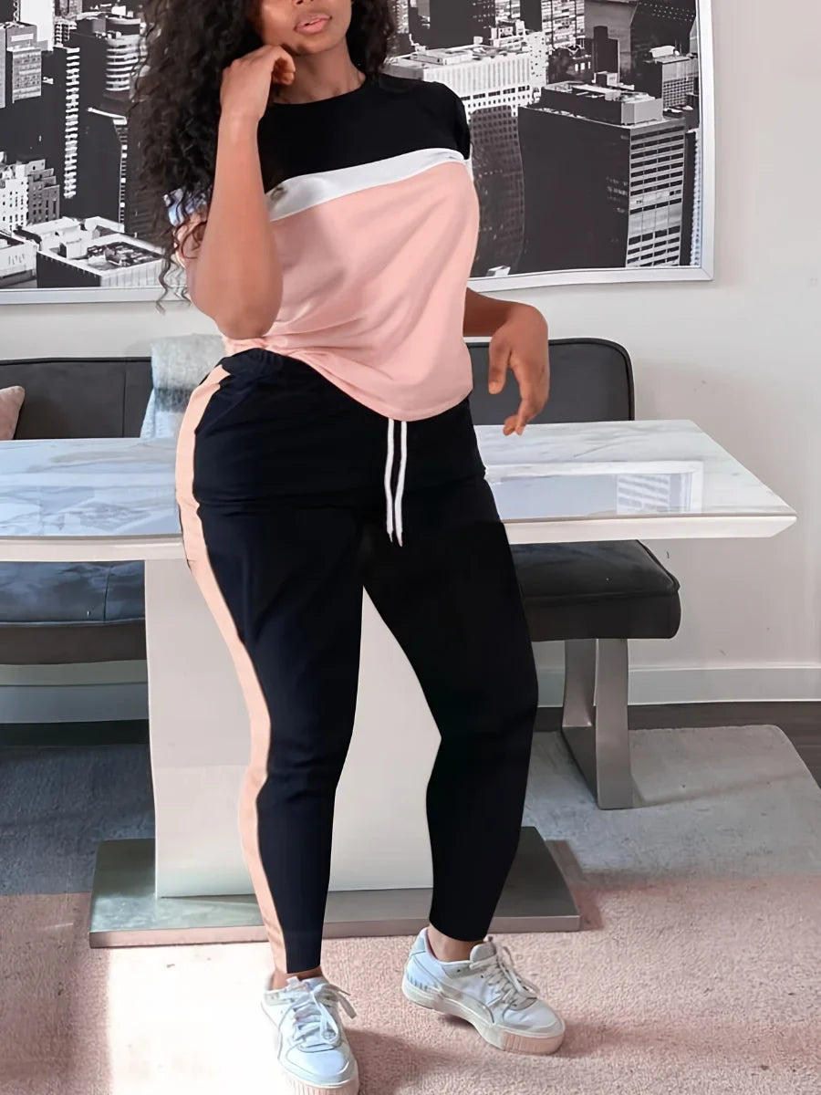 Frau in rosa-schwarzem Jogginganzug vor modernem Tisch, Stadtbild im Hintergrund.