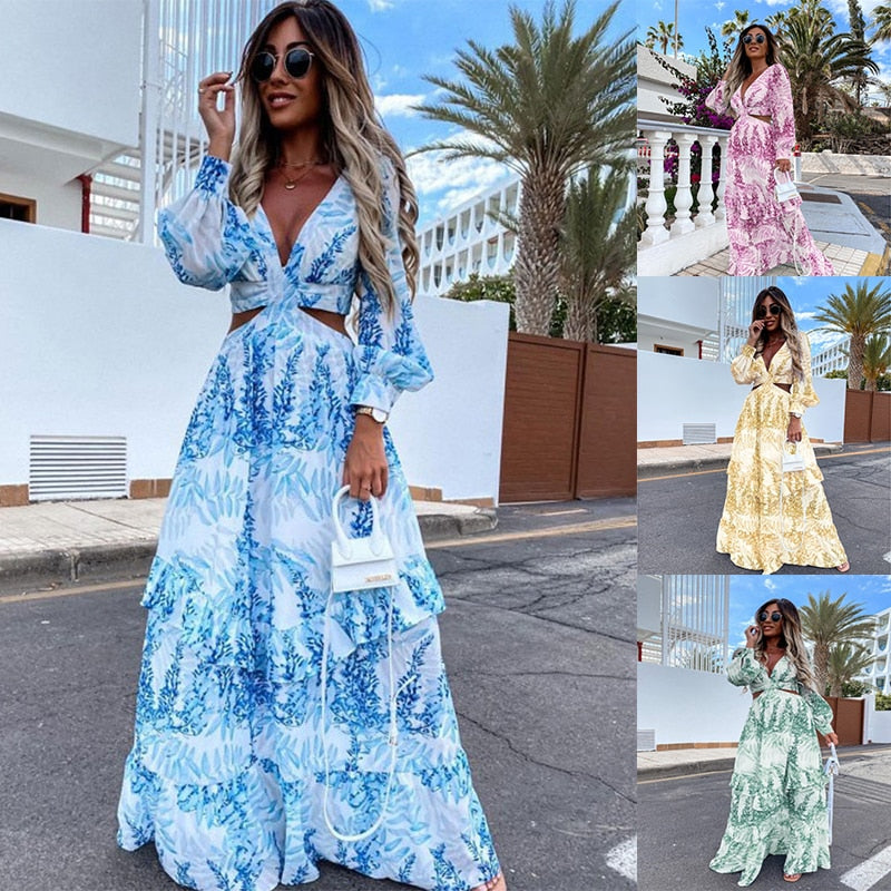 Frau in blauem Maxikleid mit Blumenmuster, Sonnenbrille, Handtasche, Straße, Palmen im Hintergrund.
