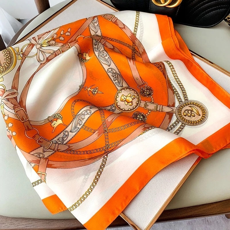 Orange-weißer Seidenschal mit Ketten- und Gürtelmuster auf Tisch, luxuriöses Accessoire.