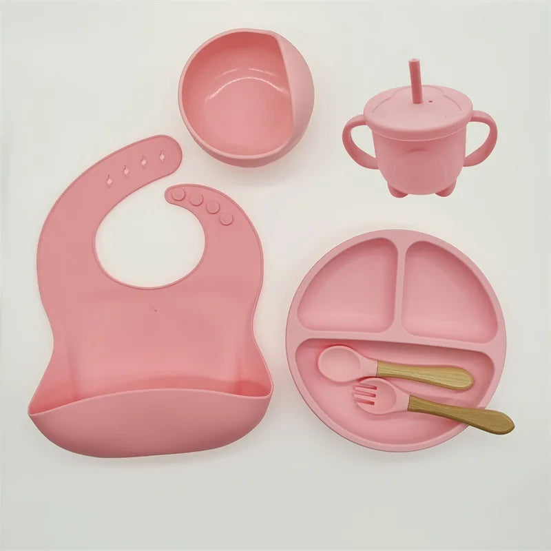 Rosa Silikon-Babygeschirr-Set mit Lätzchen, Teller, Schüssel, Becher und Besteck.
