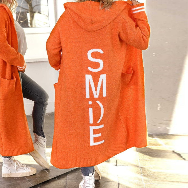 Frau in orangefarbenem Strickmantel mit "SMILE"-Aufdruck, lässige Mode, Herbstbekleidung.