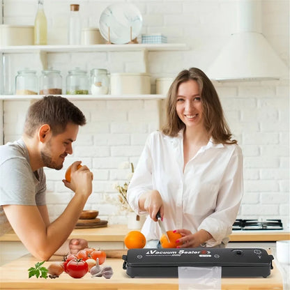 Paar in moderner Küche mit Vakuumierer, frisches Obst und Gemüse, weißes Interieur.