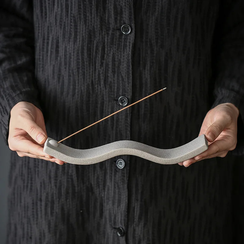 Person hält grauen Keramik-Räucherstäbchenhalter, wellenförmig, minimalistisch, modern.