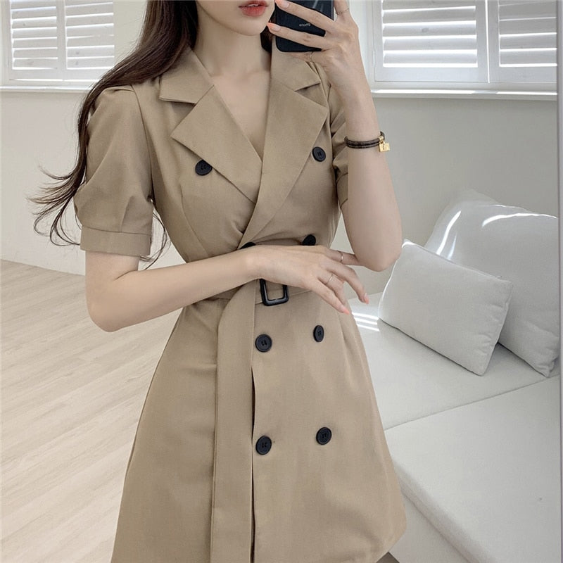 Frau in beigem Trenchcoat-Kleid, doppelte Knopfleiste, elegantes Design, modernes Wohnzimmer.