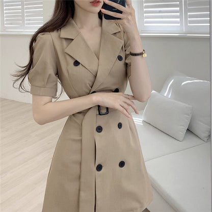 Frau in beigem Trenchcoat-Kleid, doppelte Knopfleiste, elegantes Design, modernes Wohnzimmer.