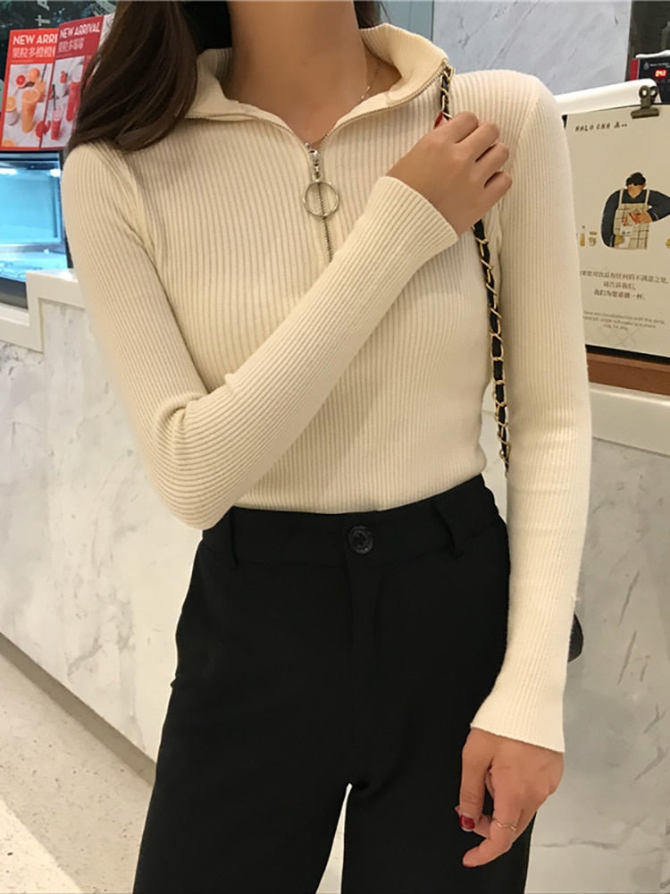 Frau in cremefarbenem Strickpullover mit Reißverschluss, schwarze Hose, modisch, elegant.