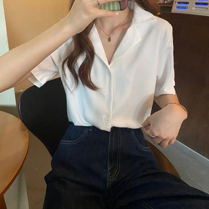 Frau in weißer Bluse und blauer Jeans, sitzt an Tisch, Smartphone in der Hand.