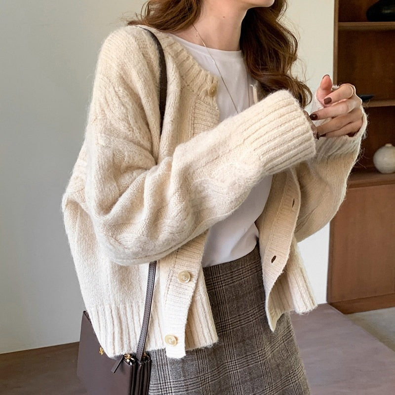 Frau trägt cremefarbene Strickjacke, weiße Bluse, karierter Rock, braune Tasche.