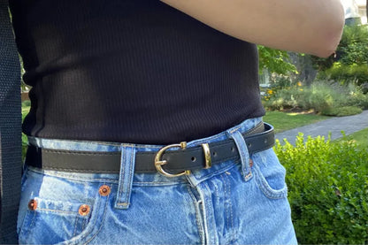 Schwarzer Ledergürtel mit einfacher Metallschnalle, getragen zu blauer Jeans.
