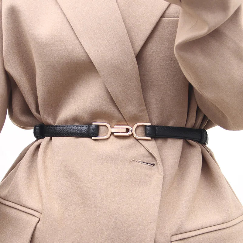 Schwarzer, verstellbarer Ledergürtel mit goldener Schnalle auf beigem Blazer.