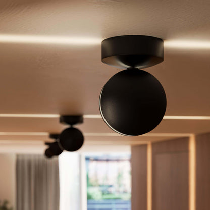 Närbild på en svart rund lampa i taket med ljusstrimmor längs taket och ytterligare en lampa suddig i bakgrunden. 11