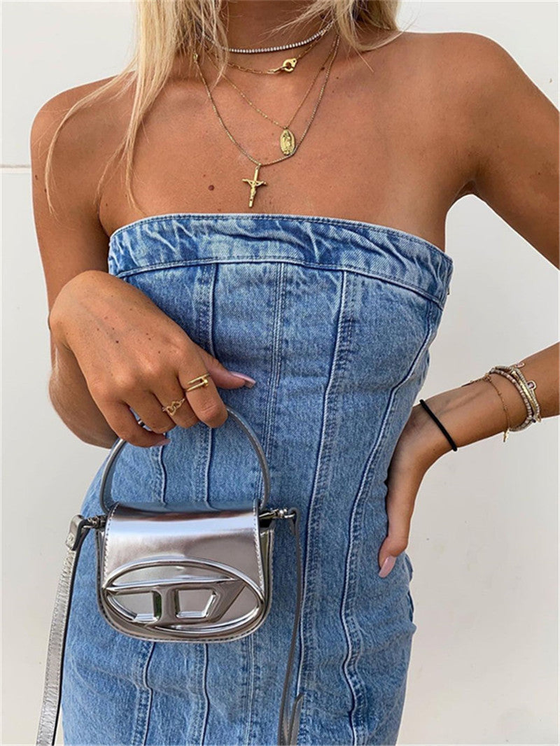 Frau in trägerlosem Jeanskleid mit silberner Handtasche und Schmuck, modisch, elegant.