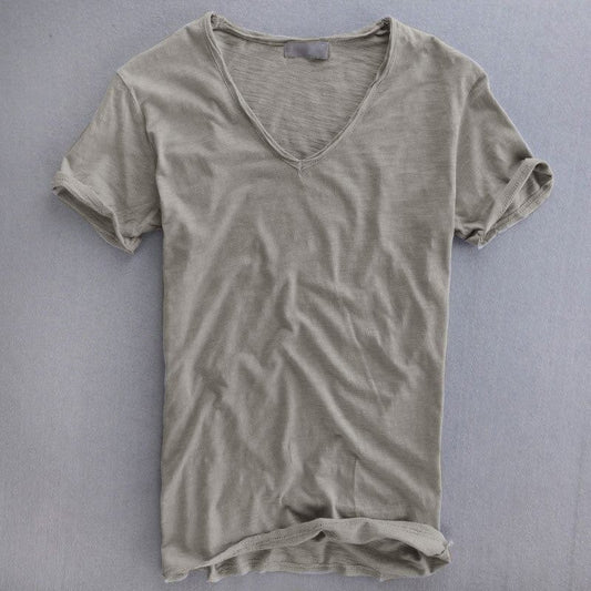Kortärmad v-ringad t-shirt i ljusgrå, utbredd platt mot grå bakgrund, med uppvikta ärmslut och texturerat tyg. 1