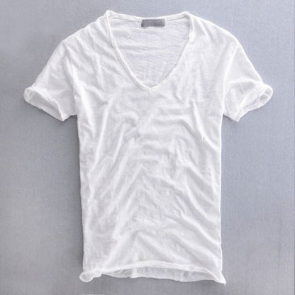Vit kortärmad v-ringad t-shirt liggande platt med uppvikta ärmar och råkantad nederkant mot grå bakgrund. 2