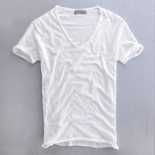 Vit kortärmad v-ringad t-shirt liggande platt med uppvikta ärmar och råkantad nederkant mot grå bakgrund. 2