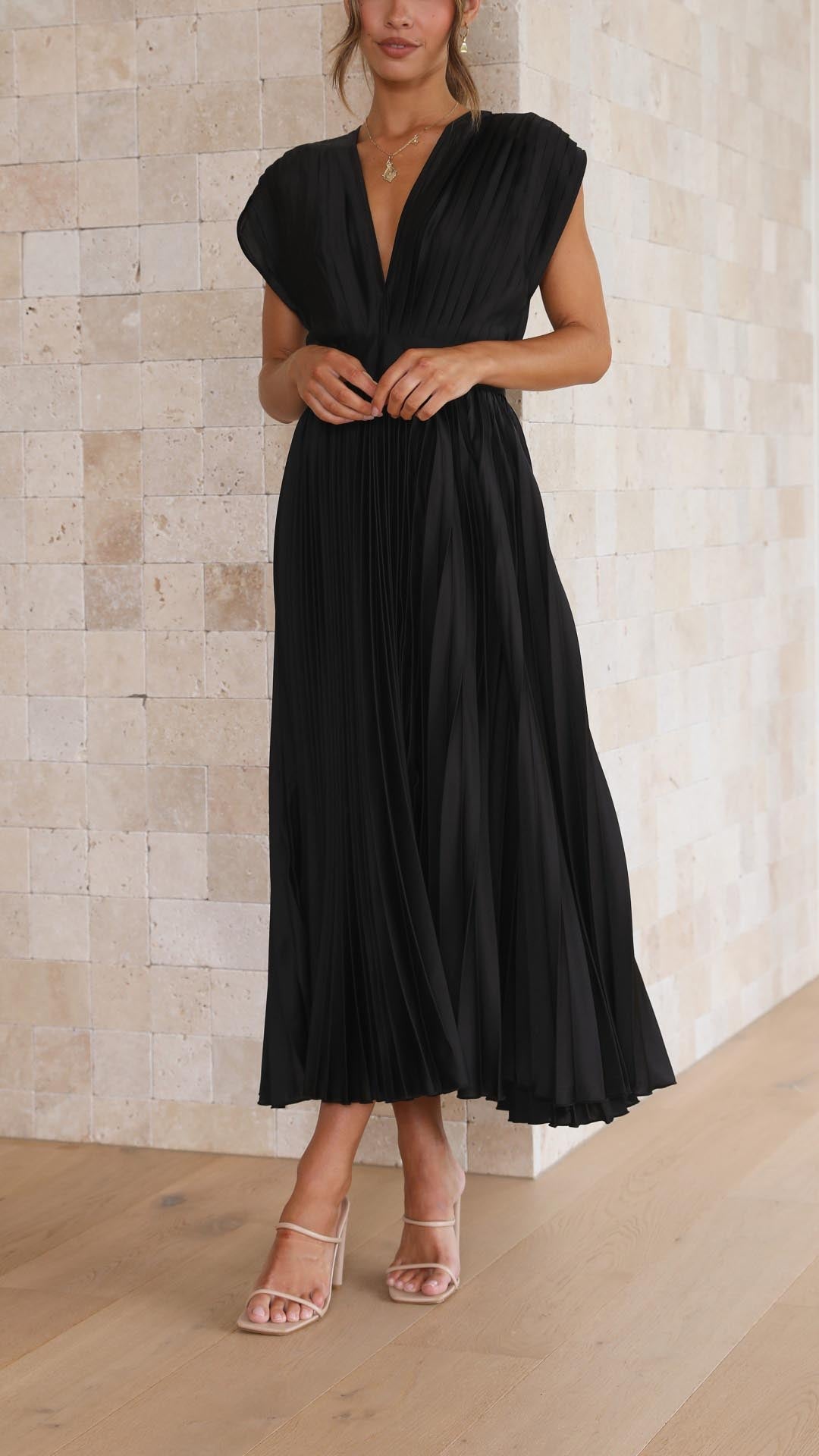 Frau in schwarzem, plissiertem Kleid vor beiger Steinwand, elegante Mode, Sommerkleid.