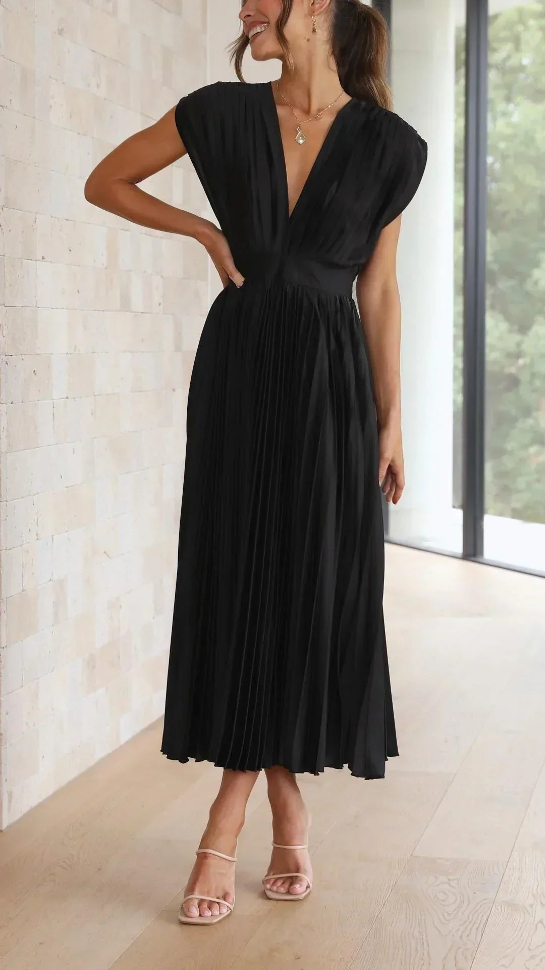 Frau in elegantem, schwarzem, plissiertem Maxikleid aus Chiffon, ärmellos, V-Ausschnitt.