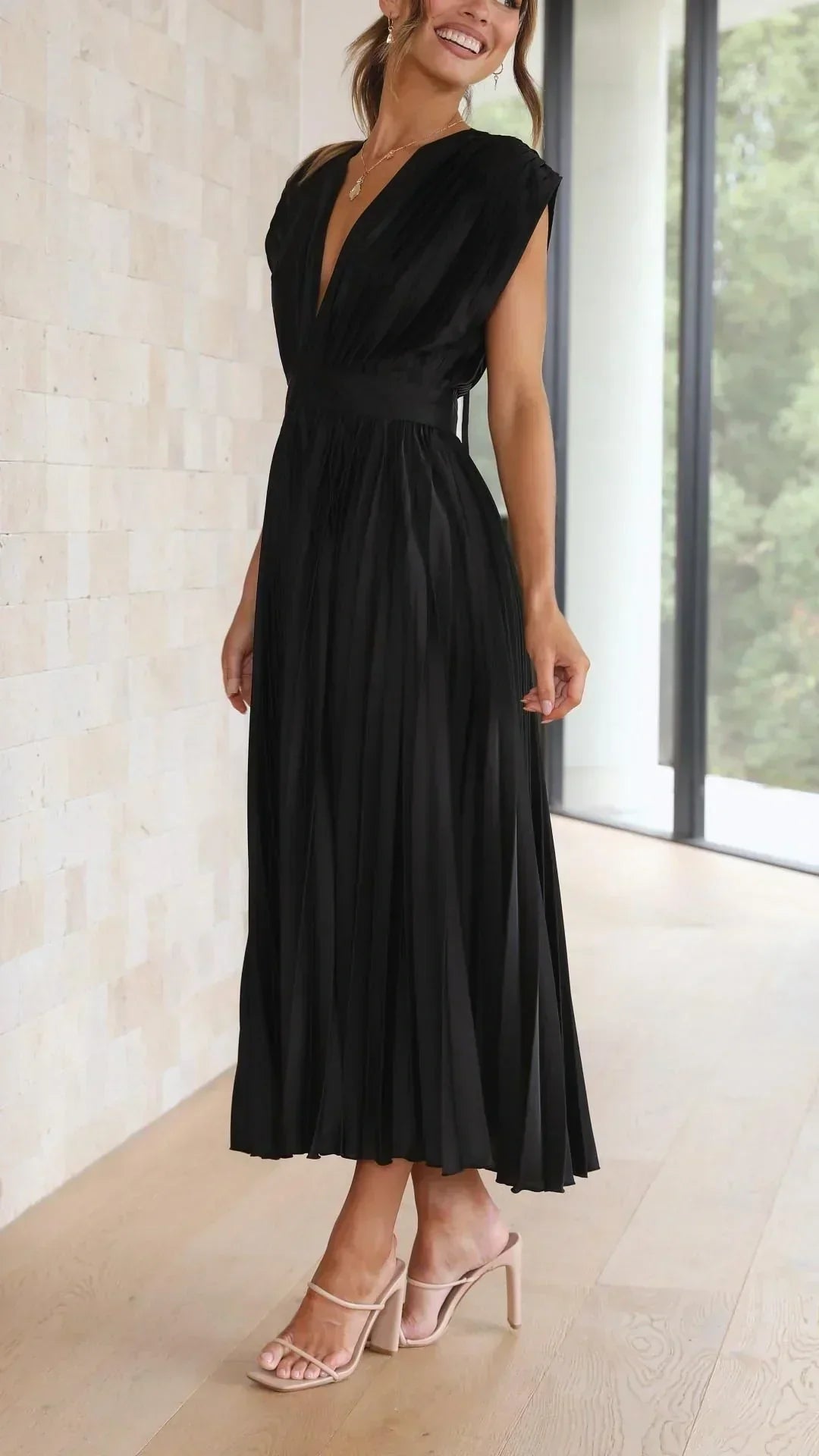 Frau in elegantem, schwarzem, plissiertem Maxikleid aus Chiffon, stehend in modernem Raum.