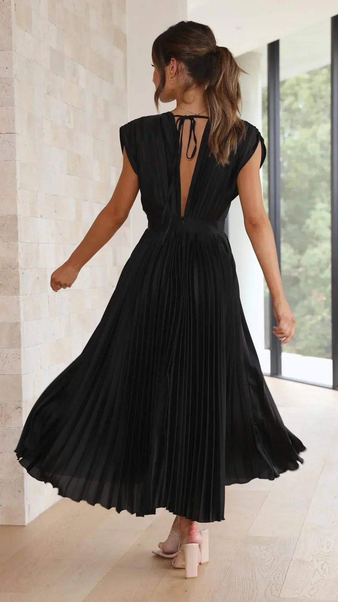 Frau in schwarzem, plissiertem Maxikleid, Rückansicht, elegantes Design, Innenraum.