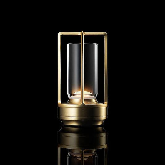 Lampa med guldfärgad metallram och bas, tänd mot svart bakgrund med reflektion i underlaget, sedd framifrån. 1