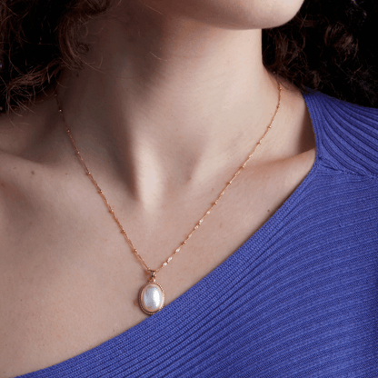 Frau mit goldener Halskette und Perlenanhänger, blaues Oberteil, eleganter Schmuck.