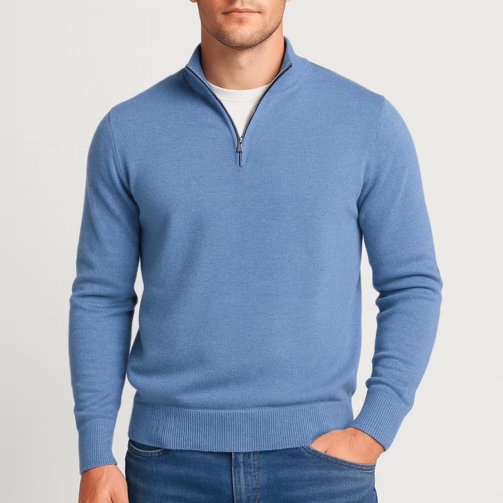 Man i blå stickad tröja med halv dragkedja, vit t-shirt under och en hand i jeansfickan. 13