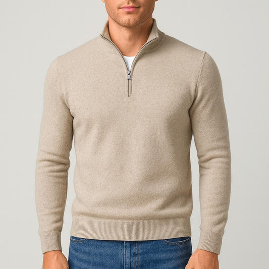Man i beige stickad tröja med halv dragkedja och ribbad avslutning, burna med jeans mot ljus bakgrund. 1