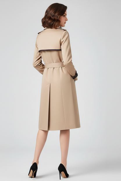 Baksidan av den beige trenchcoaten på modell, med axelstycke, skärp i midjan och veck mitt bak i kjolpartiet. 4