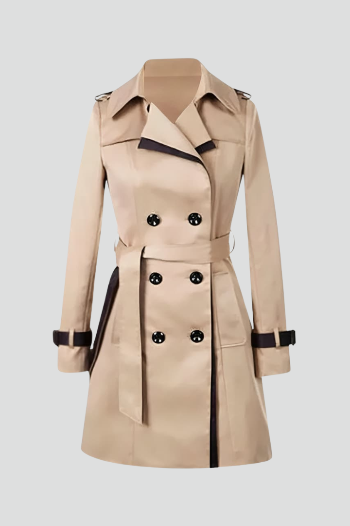Beige dubbelknäppt trenchcoat med mörka kantlinjer, knytskärp och remmar vid ärmslut, fotograferad ensam mot ljus bakgrund. 1