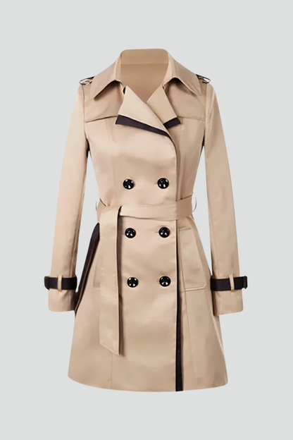 Beige dubbelknäppt trenchcoat med mörka kantlinjer, knytskärp och remmar vid ärmslut, fotograferad ensam mot ljus bakgrund. 1