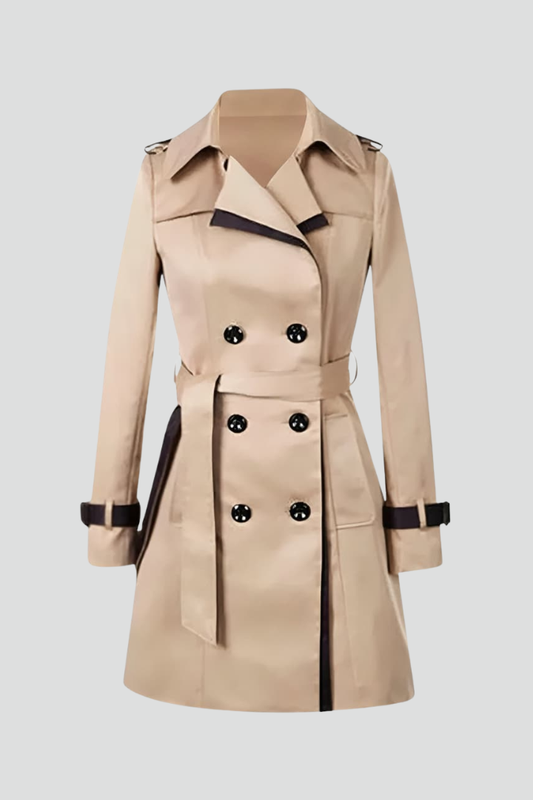 Beige dubbelknäppt trenchcoat med mörka kantlinjer, knytskärp och remmar vid ärmslut, fotograferad ensam mot ljus bakgrund. 1