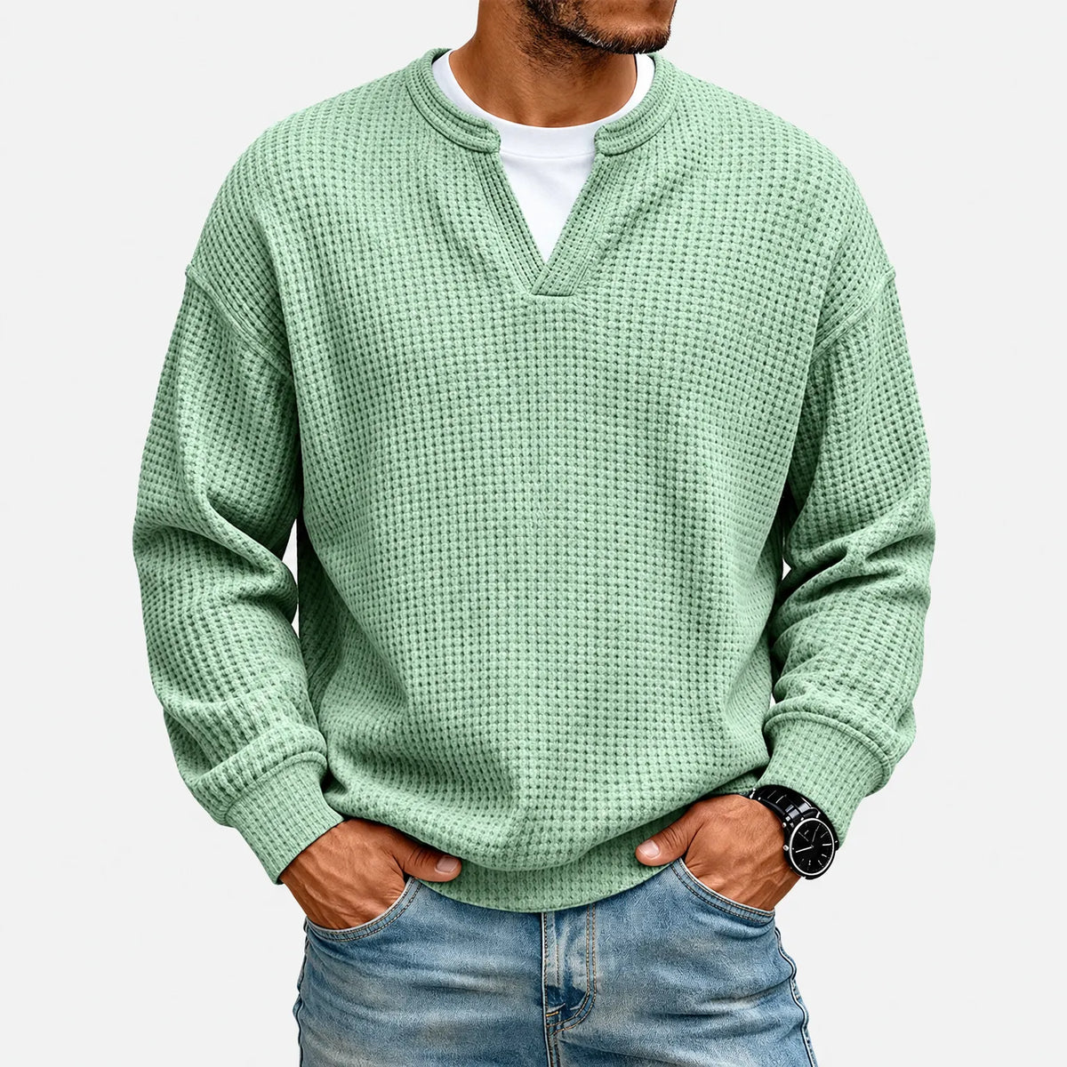 Samma mintgröna våffelstickade tröja på modell mot neutral bakgrund, med vit t-shirt under och jeans 2