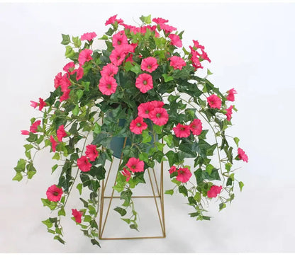 Rosa blommor och gröna slingrande blad hänger över kanten på en blågrön kruka på ett guldfärgat metallställ. 3