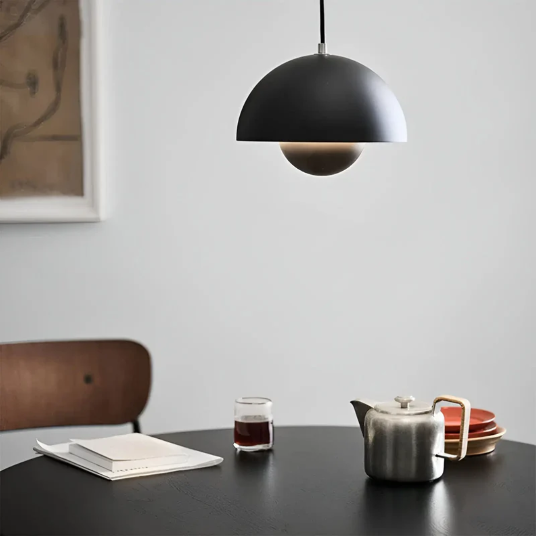 Schwarze Pendelleuchte über Tisch mit Teekanne, Glas, Notizbuch, modern, minimalistisch.