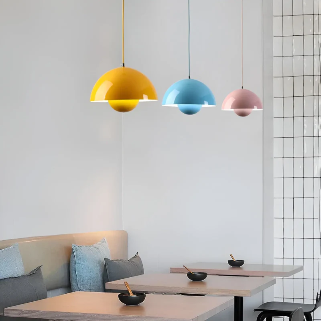 Drei bunte Pendelleuchten, gelb, blau, rosa, über modernen Esstischen in minimalistischem Raum.