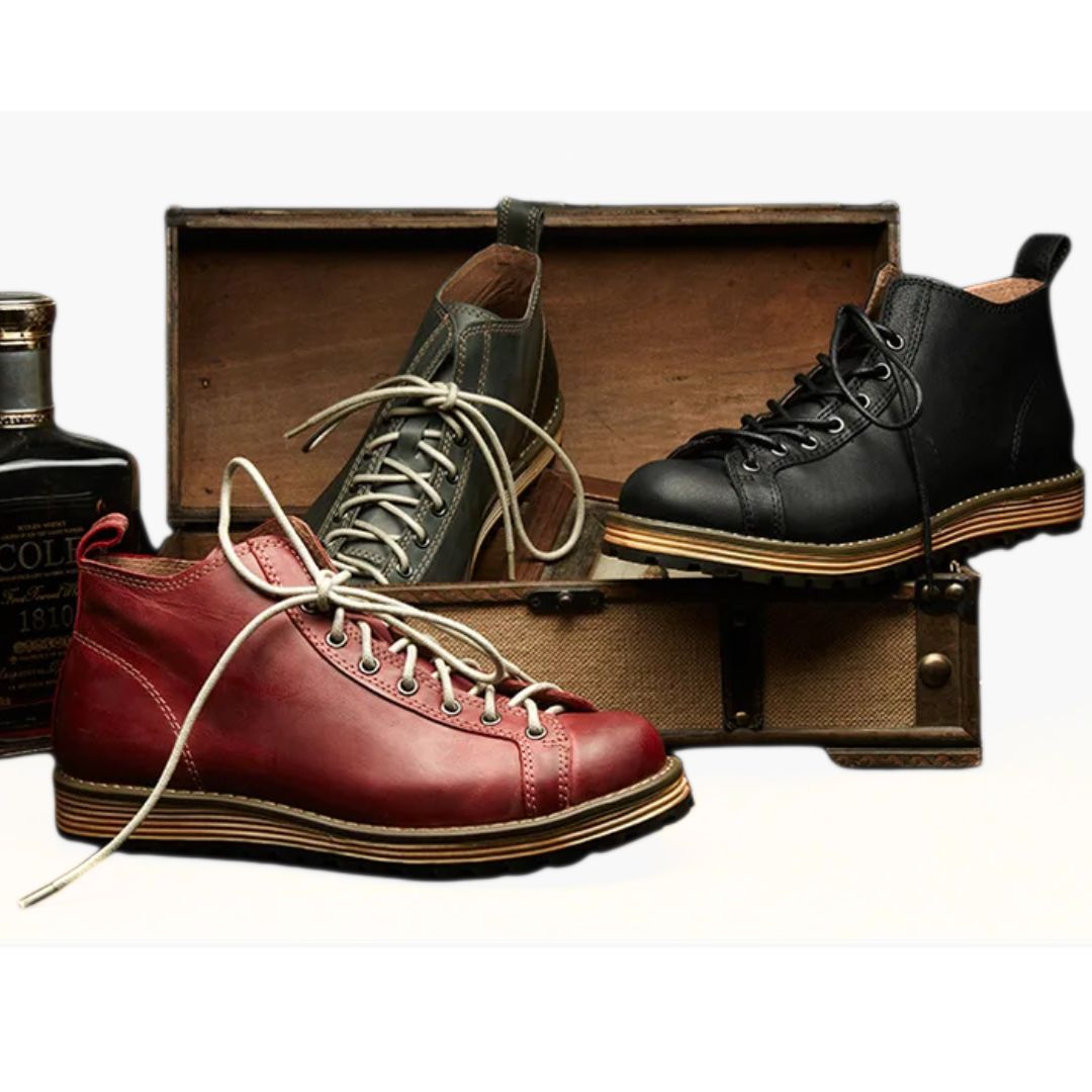 Drei Lederstiefel in Rot, Schwarz und Grau vor Holzkiste, modisch und robust.