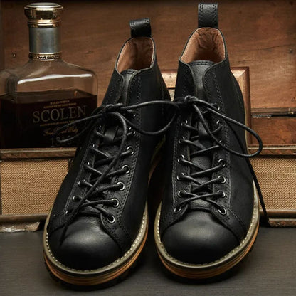 Schwarze Lederstiefel mit Schnürung, Herrenmode, vor Whiskyflasche, rustikaler Hintergrund.