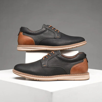 Schwarze und braune Herrenschuhe aus Leder, elegant, mit Schnürsenkeln, auf weißem Podest.