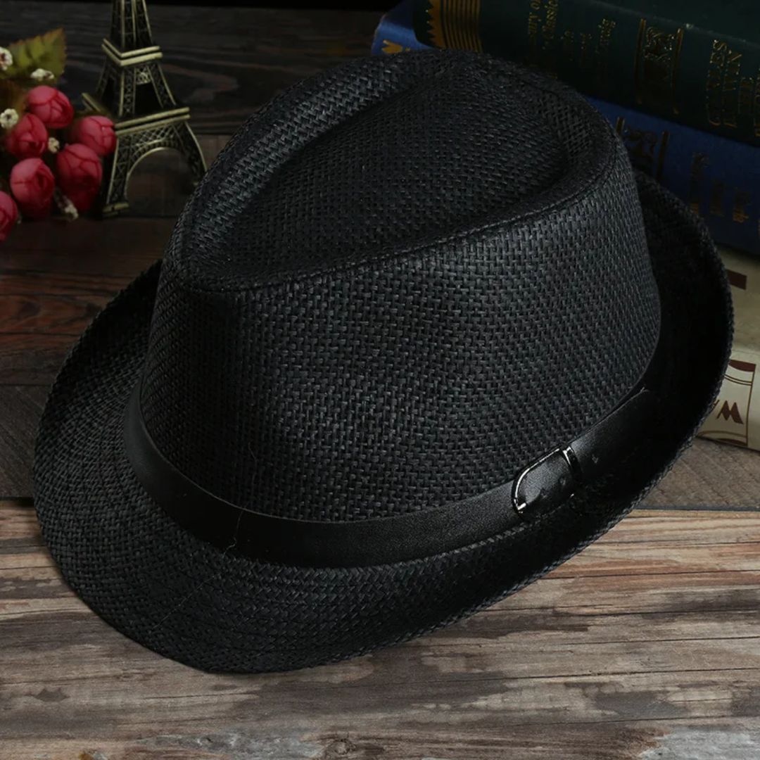 Schwarzer Fedora-Hut aus Stroh mit schwarzem Band auf Holztisch, dekorative Bücher im Hintergrund.
