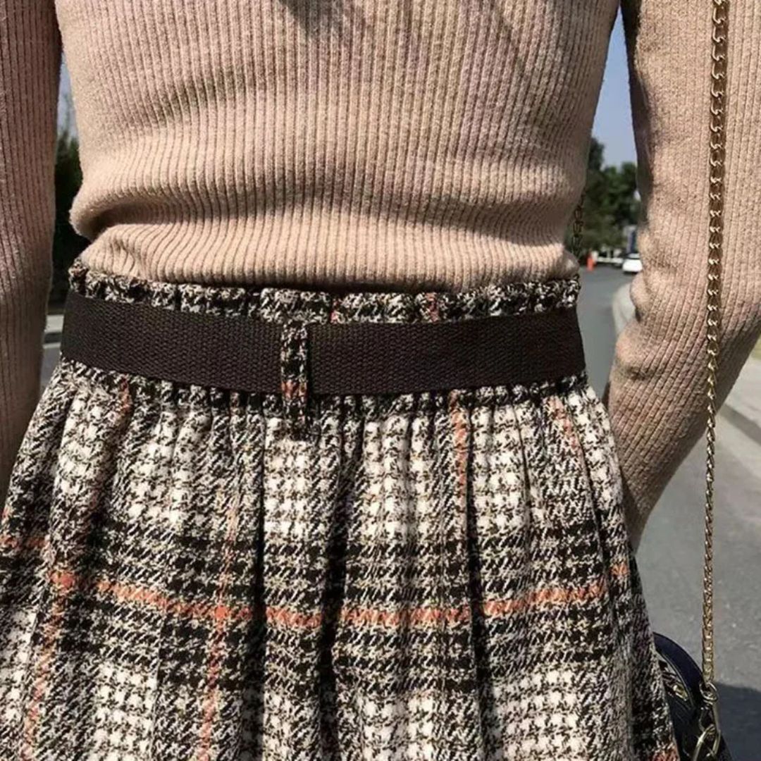 Damenmode: Beiger Pullover, karierter Rock, schwarzer Gürtel, Herbstoutfit, Straßenhintergrund.