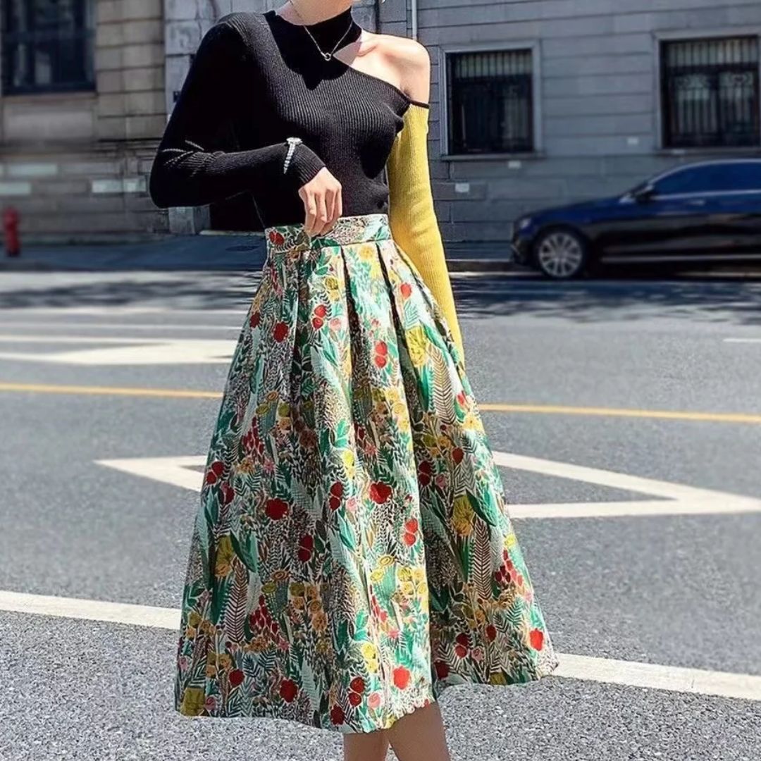 Frau in schwarzem Pullover und bunter Blumenrock auf Straße, modisch, urbaner Stil.